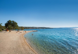 Zonnig strand en helderblauwe zee bij Aminess Gaia Green Villas Njivice in Kroatië op een stralende dag.