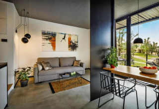 Moderne stacaravan woonkamer en eetgedeelte met grote ramen, stijlvolle inrichting en uitzicht op tuin.