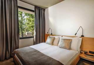 Camera moderna alle Aminess Gaia Green Villas Njivice, Croazia, con letto matrimoniale e vista sul verde.