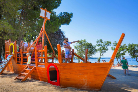 Bambini che giocano su un parco giochi a forma di nave pirata vicino alla spiaggia di Aminess Gaia Green Villas in Croazia.