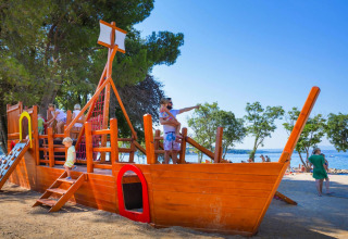 Bambini che giocano su un parco giochi a forma di nave pirata vicino alla spiaggia di Aminess Gaia Green Villas in Croazia.