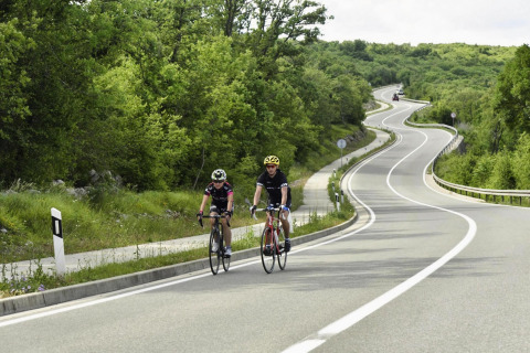 Twee fietsers rijden op een kronkelende weg omringd door groen nabij Njivice, Kroatië.