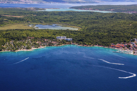 Vista aerea di Aminess Gaia Green Villas Njivice in Croazia, circondata da bosco e mare turchese brillante.