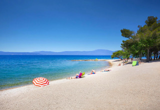 Spiaggia presso Aminess Gaia Green Villas Njivice, Croazia, con bagnanti, mare blu e alberi vicini.