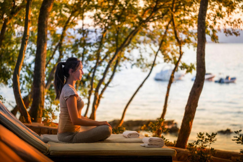 Vrouw mediteert op een terras met uitzicht op zee bij zonsondergang bij Aminess Gaia Green Villas in Kroatië.