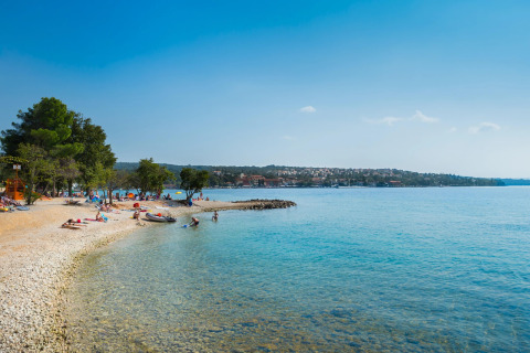 Spiaggia presso Aminess Gaia Green Villas Njivice in Croazia con acqua limpida e persone che si rilassano.