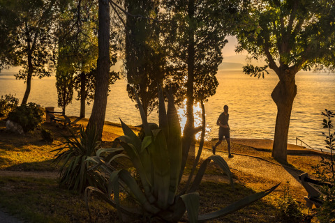 Zonsondergang bij zee bij Aminess Gaia Green Villas Njivice, Kroatië, met een hardloper en planten.