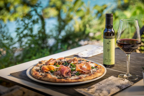 Pizza, olio d’oliva e vino rosso all’aperto alle Aminess Gaia Green Villas in Croazia, vista sul verde.