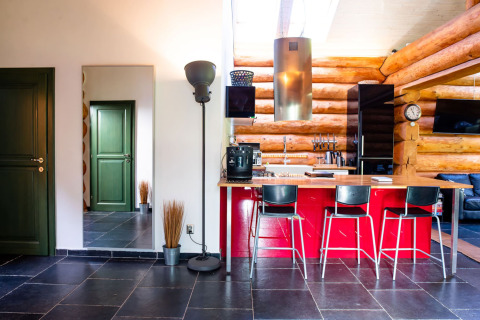 Cucina moderna in chalet ceco con isola rossa, sgabelli neri, pareti in tronchi e porte verdi.