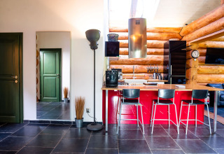 Cucina moderna in chalet ceco con isola rossa, sgabelli neri, pareti in tronchi e porte verdi.