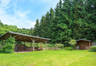 Zona relax coperta e casetta di legno accanto a un bosco e prato verde, presso uno chalet in Repubblica Ceca.