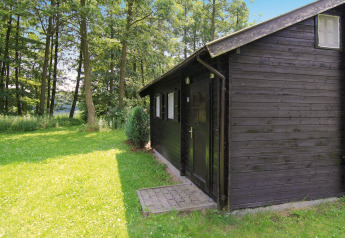 Sort træhytte på 30 m² med grøn græsplæne og skov baggrund, optaget i Tyskland på en solrig dag.