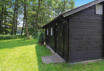 Cabaña de troncos negra de 30 m² con césped verde y bosque, tomada en Alemania en un día soleado.