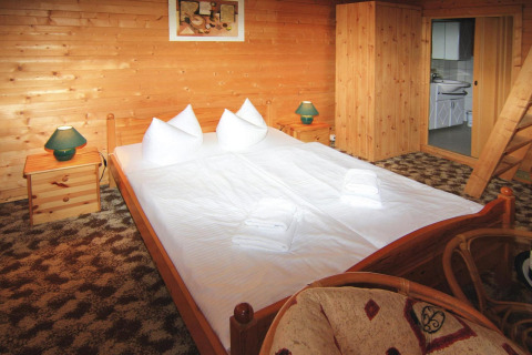 Cozy interior of a 30 m² log cabin in Germany, featuring a double bed, wooden furniture, and lamps.