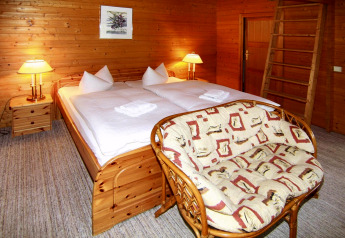 Hyggeligt soverum i en træhytte med dobbeltseng, sofa, trævægge og varmt lys, Log cabin 30 m², Tyskland.
