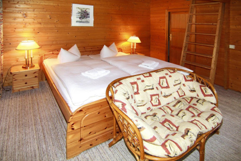 Acogedor dormitorio de cabaña de madera con cama doble, sofá y lámparas cálidas, Log cabin 30 m², Alemania.
