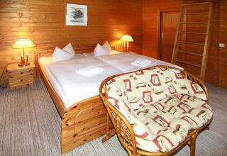 Acogedor dormitorio de cabaña de madera con cama doble, sofá y lámparas cálidas, Log cabin 30 m², Alemania.