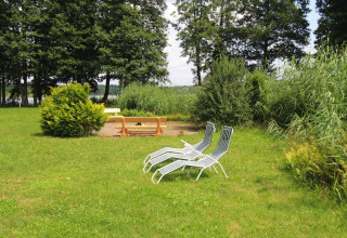 Outdoor area at a log cabin in Germany featuring two lounge chairs, a bench, and lush greenery.