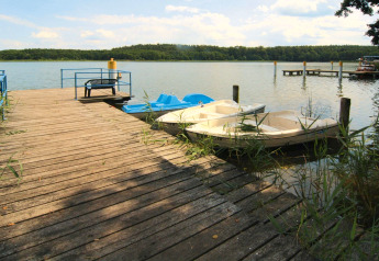 Holzsteg mit Bänken und Ruderbooten an einem ruhigen See nahe Log cabin «30 m²» in Deutschland.