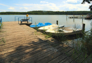 Muelle de madera con bancos y botes en un lago tranquilo, cerca de Log cabin «30 m²» en Alemania.
