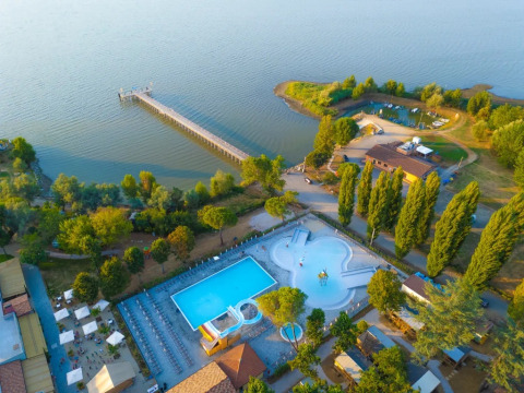 Vista aerea del Trasimeno Glamping Resort in Umbria, Italia, con piscina, alberi e lago con pontile.
