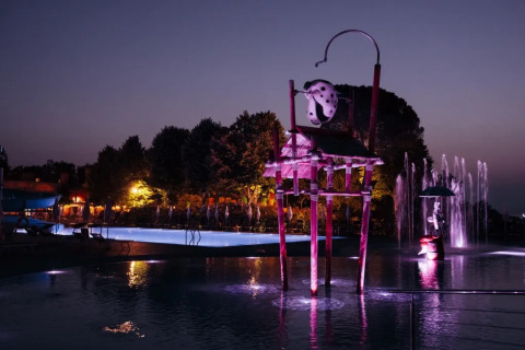 Piscina illuminata con figure fantasiose al Trasimeno Glamping Resort in Umbria, Italia, al tramonto.