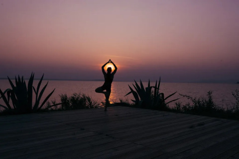 Persona che pratica yoga al tramonto sul lago presso Trasimeno Glamping Resort in Umbria, Italia.