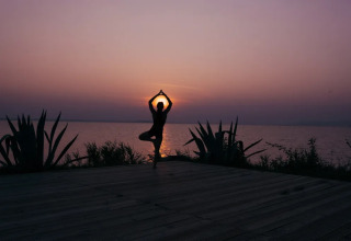 Person practicing yoga at sunset by the lake at Trasimeno Glamping Resort in Umbria, Italy.