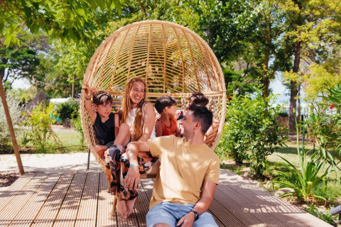 Famiglia felice si rilassa su un'altalena di vimini al Trasimeno Glamping Resort in Umbria, Italia.
