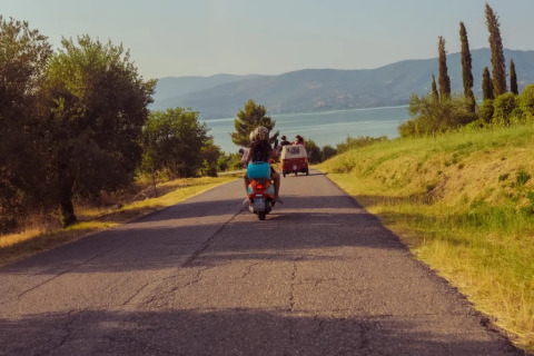 Due persone su uno scooter seguono un furgone rosso lungo una strada panoramica vicino a Sant Arcangelo di Magione, Umbria.