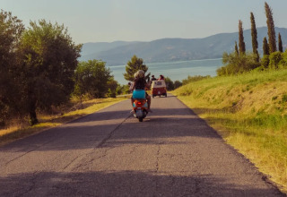 Two people on a scooter follow a red van along a scenic road near Sant Arcangelo di Magione, Umbria, Italy.