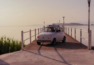 A classic car is parked on a lakeside pier near Sant Arcangelo di Magione, Umbria, Italy, at sunset.