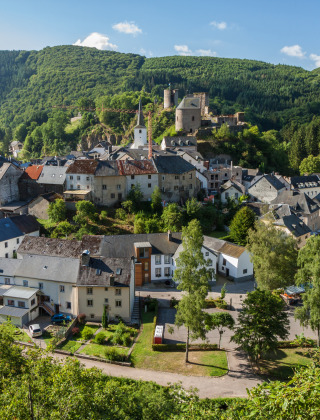 Scenic view over a charming village with a castle and forested hills, near a glamping holiday park.