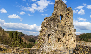 Ruins of a stone wall at a holiday park offering glamping, set among lush hills and forests under blue sky.