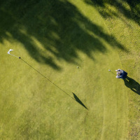 Vista aérea de una persona jugando golf en el green de un parque vacacional con opciones de glamping.