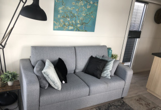 Moderne woonkamer in Marina Parcs Amsterdam met grijze sofa, kussens, vloerlamp en kunst aan de muur.