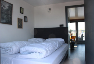 Een moderne slaapkamer met twee bedden en witte dekens in Marina Parcs Amsterdam, vakantiepark in Noord-Holland.