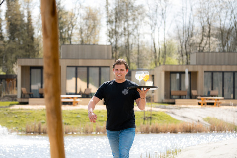 Een ober loopt buiten met drankjes op een dienblad bij Resort de Parel, een vakantiepark in Flevoland, Nederland.