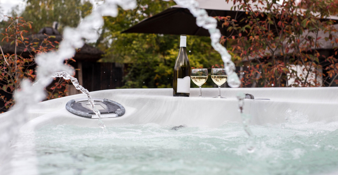Bubbelbad buiten met waterstralen, een fles wijn en glazen bij Woodz Lodges vakantiepark in België.