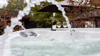 Outdoor hot tub with water jets, wine bottle, and two glasses at Woodz Lodges holiday park in Belgium.