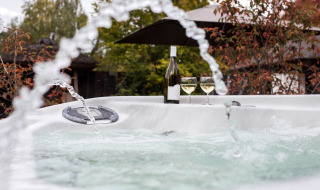 Jacuzzi exterior con chorros, botella de vino y dos copas en Woodz Lodges, parque vacacional en Bélgica.