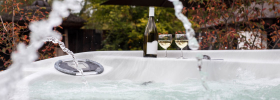 Jacuzzi exterior con chorros, botella de vino y dos copas en Woodz Lodges, parque vacacional en Bélgica.