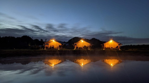 Drie verlichte glampingtenten weerspiegeld in het water bij Camping de Heerlijkheid Vorenseinde in Noord-Brabant.