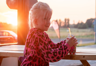 Jonge meisje geniet van een ijsje in een roze jas bij Camping de Tolbrug in Gelderland bij zonsondergang.