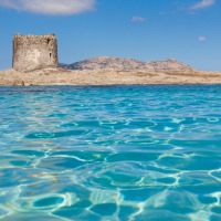 Una antigua torre de piedra se alza en la costa junto a aguas azules cerca de Vignole Mare SS, Cerdeña, Italia.