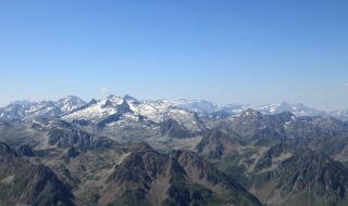 Vista panorámica de montañas nevadas y valles verdes bajo un cielo azul en un parque de glamping