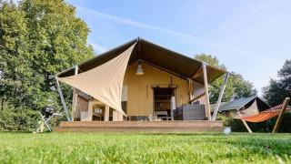 Safari-Zelt Country mit Holzterrasse, Grill und Hängematte, umgeben von grünem Rasen und Bäumen.