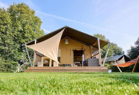Safari-Zelt Country mit Holzterrasse, Grill und Hängematte, umgeben von grünem Rasen und Bäumen.