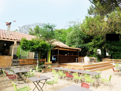 Area caffè esterna al campeggio La Vallée Heureuse con sedie colorate, tavoli e natura rigogliosa attorno.