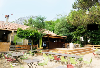 Area caffè esterna al campeggio La Vallée Heureuse con sedie colorate, tavoli e natura rigogliosa attorno.